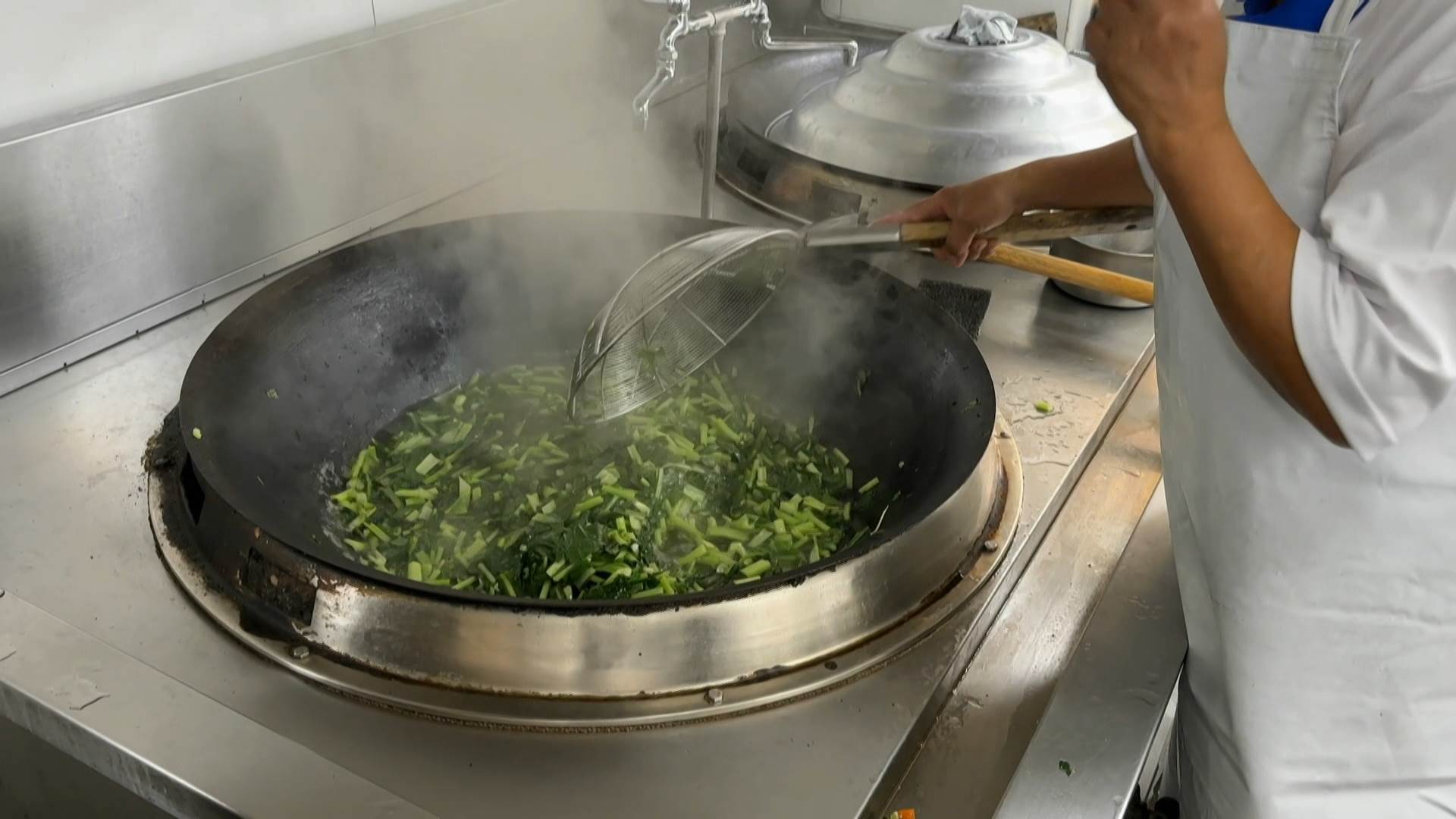 廚工阿姨不停翻炒，將新鮮青菜起鍋後分裝，讓學生們能夠趁熱享用營養午餐。（圖／東森新聞） 