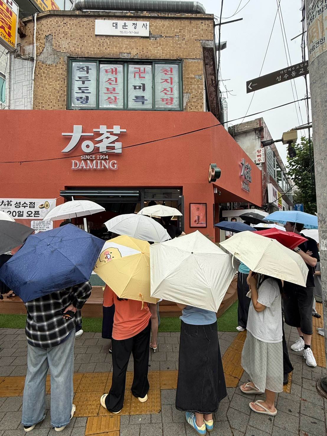 大茗首爾聖水洞店外，民眾撐傘在入口前等候，畫面可見店面招牌與候位人群。（圖／大茗本位製茶堂提供）