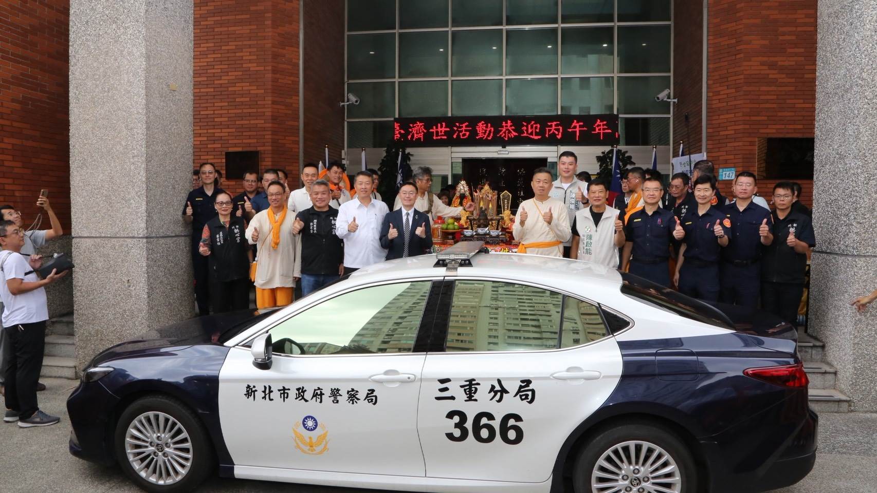 北港武德宮開基天官武財神行腳抵達三重分局,新北拱心宮、地方立委、議員及三重警方於前年捐贈的「三重分局366號」巡邏車前合影,場面熱絡溫馨。(圖/新北市政府警察局三重分局 提供)